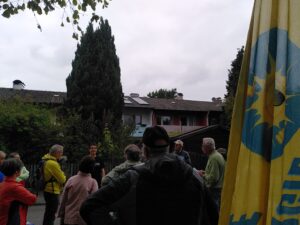 Tag der offenen Solaranlage: Die Teilnehmenden verfolgen die Erläuterungen des Betreibers. Hinter dem offenen Gartentürchen sind das Gartenhäuschen mit Steckersolargerät und das mit PV-Modulen belegte Wohnhaus zu sehen.